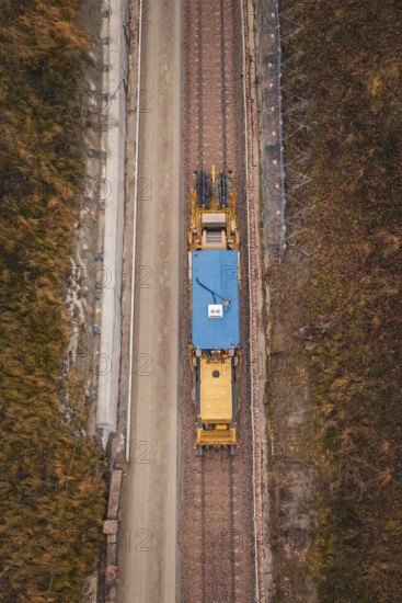 Aerial view of a yellow train during construction in a winter environment, tamping machine used on the Hermann Hessebahn construction site, Calw, Germany