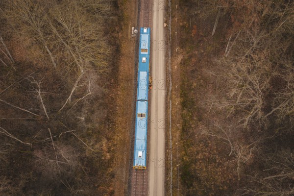 Bird's-eye view of railway line with yellow train in a wooded region, using a tamping machine at the Hermann Hessebahn construction site, Calw, Germany