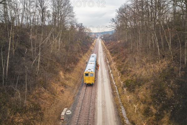 Train travels through a wintry landscape with bare trees along the tracks, using a tamping machine at the Hermann Hessebahn construction site, Calw, Germany