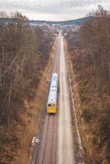 Yellow train on rails in an autumn landscape with a view of a distant city, using a tamping machine at the Hermann Hessebahn construction site, Calw, Germany