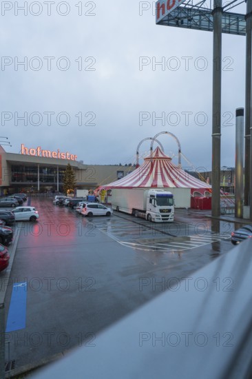 Hofmeister shopping center with circus tent and parked cars at dusk, stuffing machine used at Hermann Hessebahn construction site, Calw, Germany