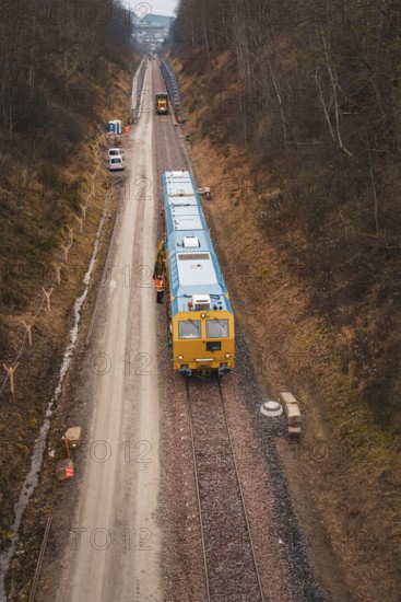Yellow train on a construction site in a wintry landscape, surrounded by trees, using a tamping machine at the Hermann Hessebahn construction site, Calw, Germany
