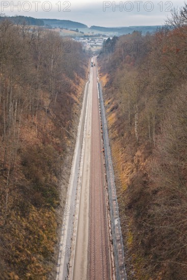A long railway line leads through a hilly autumn landscape with bare trees, using a tamping machine at the Hermann Hessebahn construction site, Calw, Germany