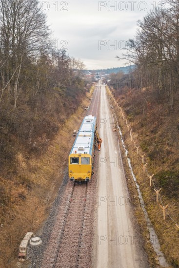 Yellow train during construction on a long rail line surrounded by bare trees, using a tamping machine at the Hermann Hessebahn construction site, Calw, Germany