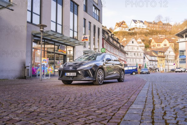 Close-up of a black car on an urban street with modern buildings in the background, MG4 electric car, Deer e-Carsharing, Calw, Germany
