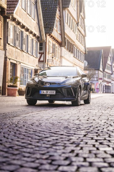 Black car drives on a cobblestone street lined with half-timbered houses and urban architecture, MG4 electric car, deer e-car sharing, Calw, Germany
