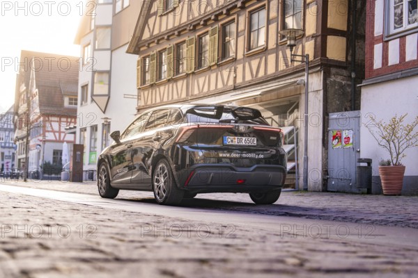 Black car from behind in a street with historic half-timbered houses in daylight, MG4 electric car, Deer e-Carsharing, Calw, Germany