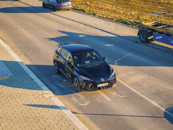 A car is parked on a wide street, illuminated by the evening sun, surrounded by open fields, MG4 electric car, Deer e-Carsharing, Calw, Germany