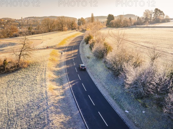 An empty road snakes through a frosty landscape in morning sunlight, MG4 electric car, deer e-car sharing, Calw, Germany