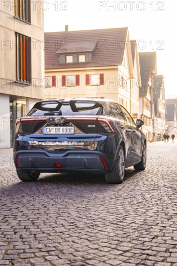 A modern car is parked on a cobblestone street in an old town at sunset, MG4 electric car, deer e-car sharing, Calw, Germany