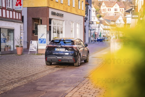 A car drives through a charming shopping street with half-timbered houses and blooming flowers, MG4 electric car, deer e-car sharing, Calw, Germany