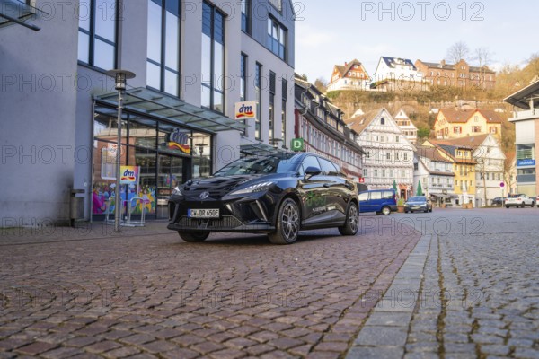 Black car in a modern city with paved streets and traditional houses in the background, MG4 electric car, Deer e-Carsharing, Calw, Germany
