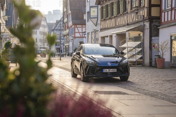 Black car in front of half-timbered houses on a picturesque street with natural light and plants in the foreground, MG4 electric car, Deer e-Carsharing, Calw, Germany