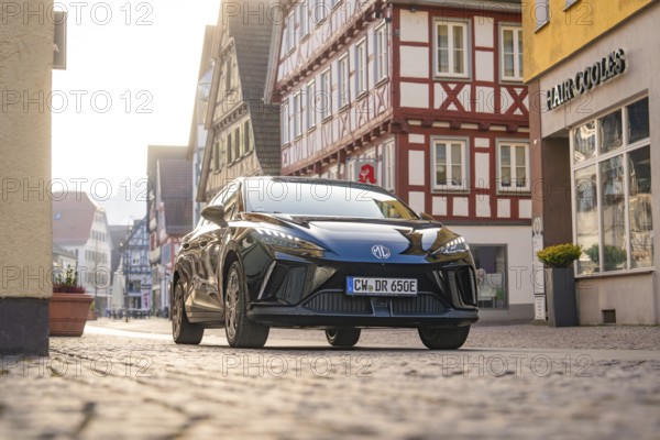 Black car on a paved street in a historic town with half-timbered houses in sunny weather, MG4 electric car, Deer e-Carsharing, Calw, Germany