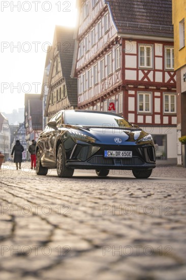 Black car on a busy paved road between half-timbered houses in an urban scene, MG4 electric car, Deer e-Carsharing, Calw, Germany