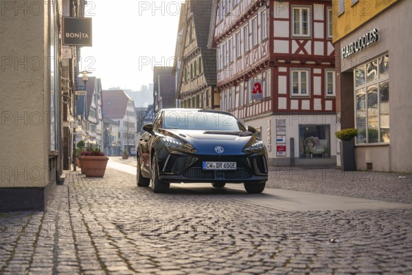 Black car drives through a paved street in a historic city environment with half-timbered houses, MG4 electric car, Deer e-Carsharing, Calw, Germany