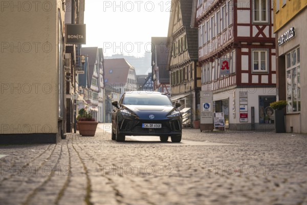 Black car in an inner city street with half-timbered houses, surrounded by a busy atmosphere in daylight, MG4 electric car, Deer e-Carsharing, Calw, Germany