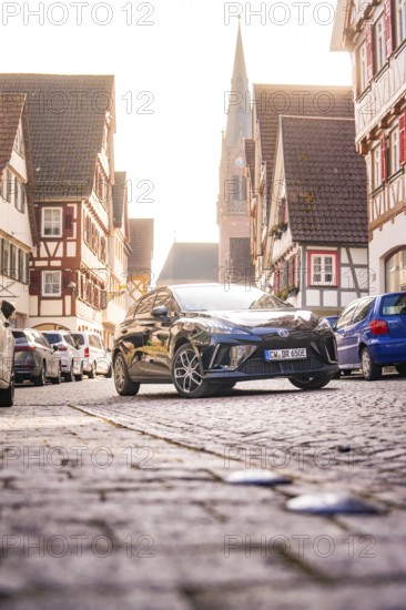 A car drives through a picturesque old town with a church in the background in sunlight, MG4 electric car, deer e-car sharing, Calw, Germany