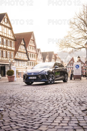 A car is parked in a paved old town and is surrounded by historic buildings and lanterns, MG4 electric car, deer e-car sharing, Calw, Germany