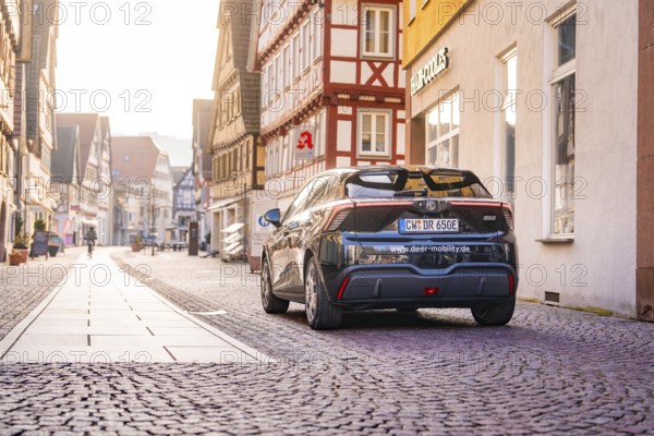 A black car on a sunny cobblestone street surrounded by half-timbered houses, MG4 electric car, deer e-car sharing, Calw, Germany