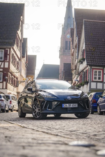 A car in a paved old town street with church and half-timbered houses, MG4 electric car, Deer e-Carsharing, Calw, Germany
