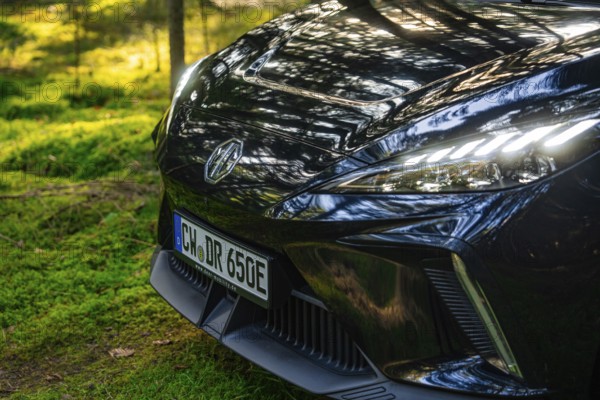 Close-up of front lights of a car with reflecting sunlight in the forest, MG4 electric car, Deer e-Carsharing, Calw, Germany