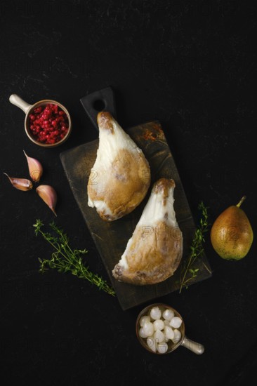 Two duck legs poached in their own rendered fat served with pear, berries, garlic and thyme on a rustic wooden board in moody light. The kitchen counter is dark, creating a focus on the fresh items in preparation for a meal