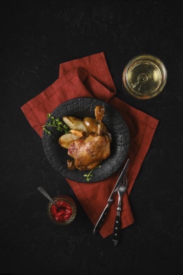 Top view of a plate with roasted duck leg along with caramelised pears and fresh thyme served with a glass of white wine and lingonberry sauce