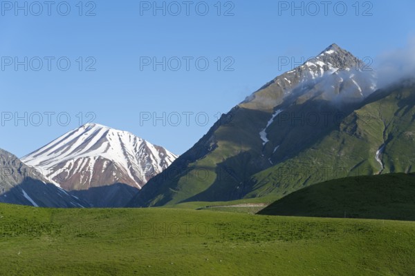Snow-capped mountains with clouds at the summit, surrounded by green hills, landscape between Kvesheti and Gudauri, Mtskheta-Mtianeti region, Georgian Military Highway, High Caucasus, Georgia