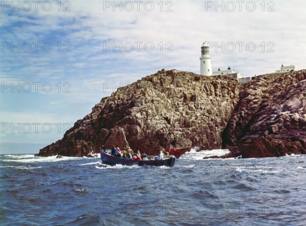 Tour boat passing rocky cliffs at Round Island lighthouse, Isles of Scilly, Cornwall, England, UK 1960s