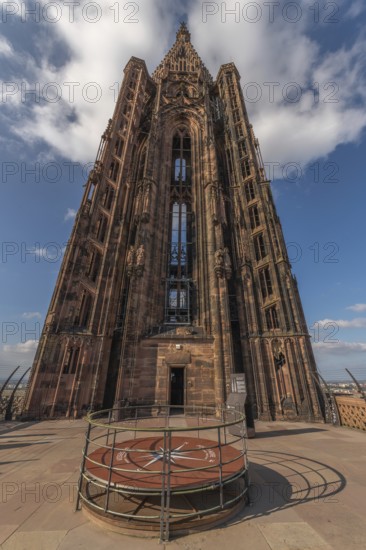 Visitors stand on a platform around the clock and admire Strasbourg Cathedral. The sky is blue with a few clouds. The architecture of the cathedral is impressive. Bas Rhin, Alsace, France