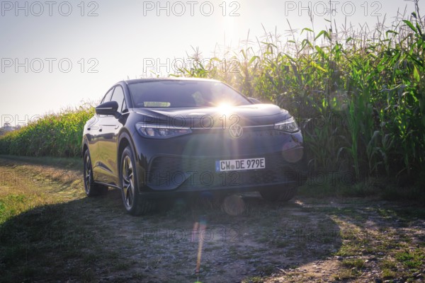 Black car on a dirt road next to a corn field with bright sunlight on the hood, VW ID5 electric car, deer e-car sharing, Calw, Germany