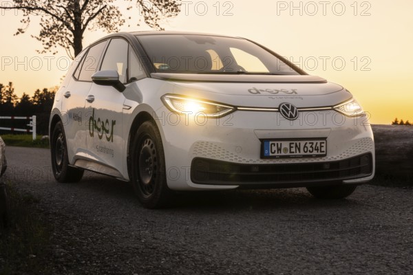 Car on country road at dusk with glowing headlights, VW ID3 electric car, deer e-car sharing, Calw, Germany