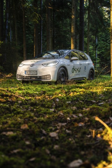 Car during the day in the forest on mossy ground, sunlight falling on the scene, VW ID3 electric car, deer e-car sharing, Calw, Germany