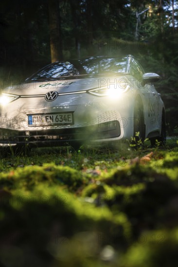 Car in the dark forest, switched on headlights illuminate the mossy ground, VW ID3 electric car, deer e-car sharing, Calw, Germany