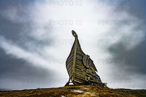 Dramatic view of an erected wooden Viking ship against a cloudy sky, sculpture by Drakkar Vardø. The Drakkar-Leviathan sculpture was built in summer 2016 by the Taibola Assemble team from Archangelsk Severodvinsk, Vardø, Finnmark, Norway