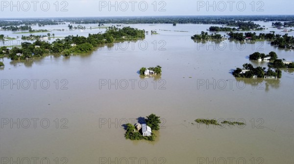 An aerial view shows widespread flooding submerging villages and farmland, with isolated homes and trees standing amid vast floodwaters