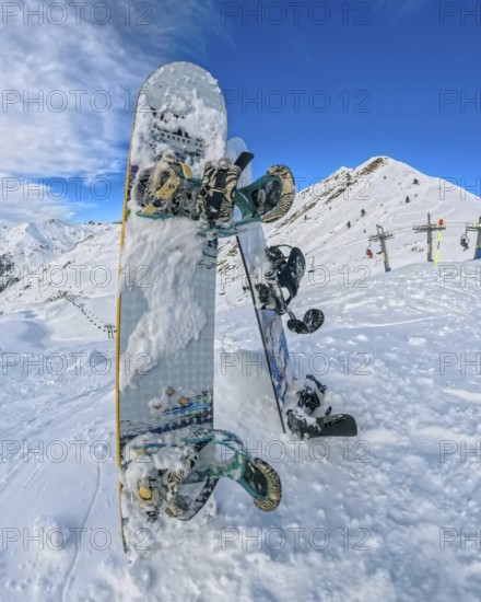 Snowboards planted upright in deep powder at a high altitude ski resort, framed by snow covered peaks, chairlifts and a clear blue skyquiet pause in winter adventure