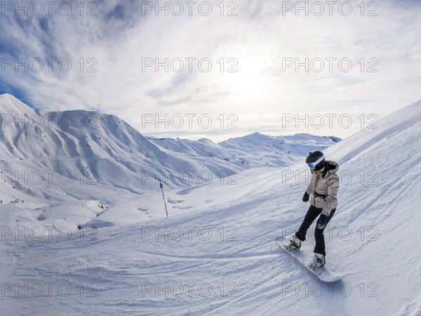 Female snowboarder in helmet and goggles carving fresh snow on a sunny alpine slope, panoramic mountain vista behind her conveying adventure, speed and open sky freedom