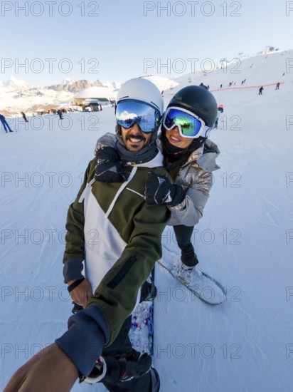Couple having fun snowboarding on a sunny winter day, enjoying their active vacation in the snow covered mountains while capturing a joyful selfie together