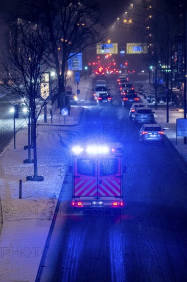 Ambulance, RTW, the Essen professional fire brigade during an emergency trip with flashing lights, winter weather, blowing snow, inner-city road traffic, Alfredstraße, B224, in Essen, North Rhine-Westphalia, Germany