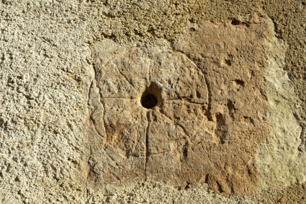 A close view showing a medieval mass dial carved into the exterior wall of St. Saturninus Church. This ancient sundial is located in Mazerier village, Allier, Auvergne Rhone Alpes, France. Europe