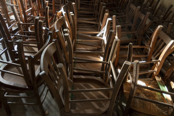 Many old wooden chairs are stacked in disarray, upside down in a church. France. Europe