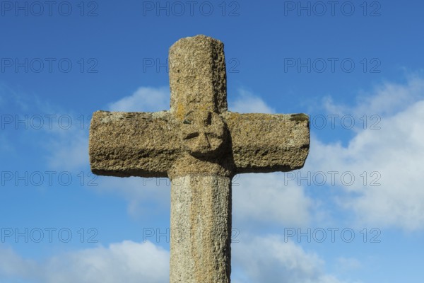 Stone cross stands tall against a bright blue sky with scattered white clouds in the background, creating a religious atmosphere