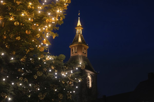 Glowing church tower next to a festively decorated Christmas tree at night, Nagold, Calw district, Black Forest, Germany