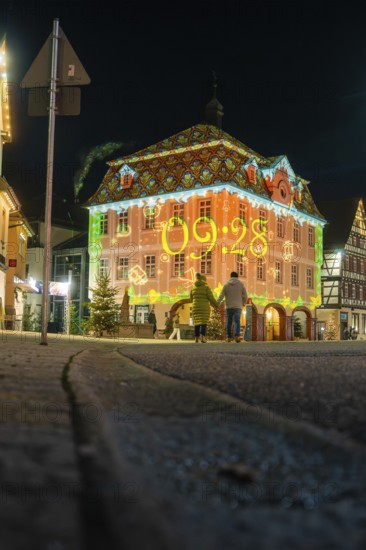 A family looks at a historic building decorated with glowing projections at night, Nagold, Calw district, Black Forest, Germany