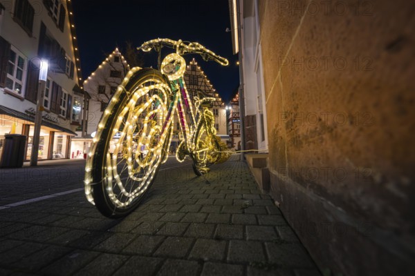 A bicycle artfully decorated with lights stands at night in the illuminated old town, Nagold, Calw district, Black Forest, Germany