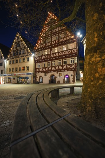 Beautiful half-timbered houses shine at night under fairy lights, captured by a curved wooden bench, Nagold, Calw district, Black Forest, Germany