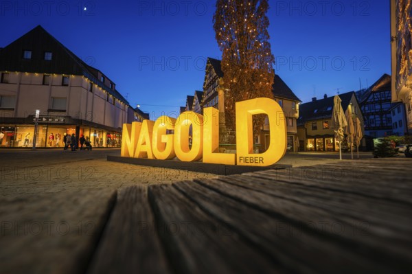 The illuminated Nagold lettering shines at dusk and creates a lively atmosphere in the city center, Nagold, Calw district, Black Forest, Germany