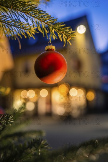 Red Christmas ball on pine branch, evening mood with blurred lights in the background, Nagold, Calw district, Black Forest, Germany